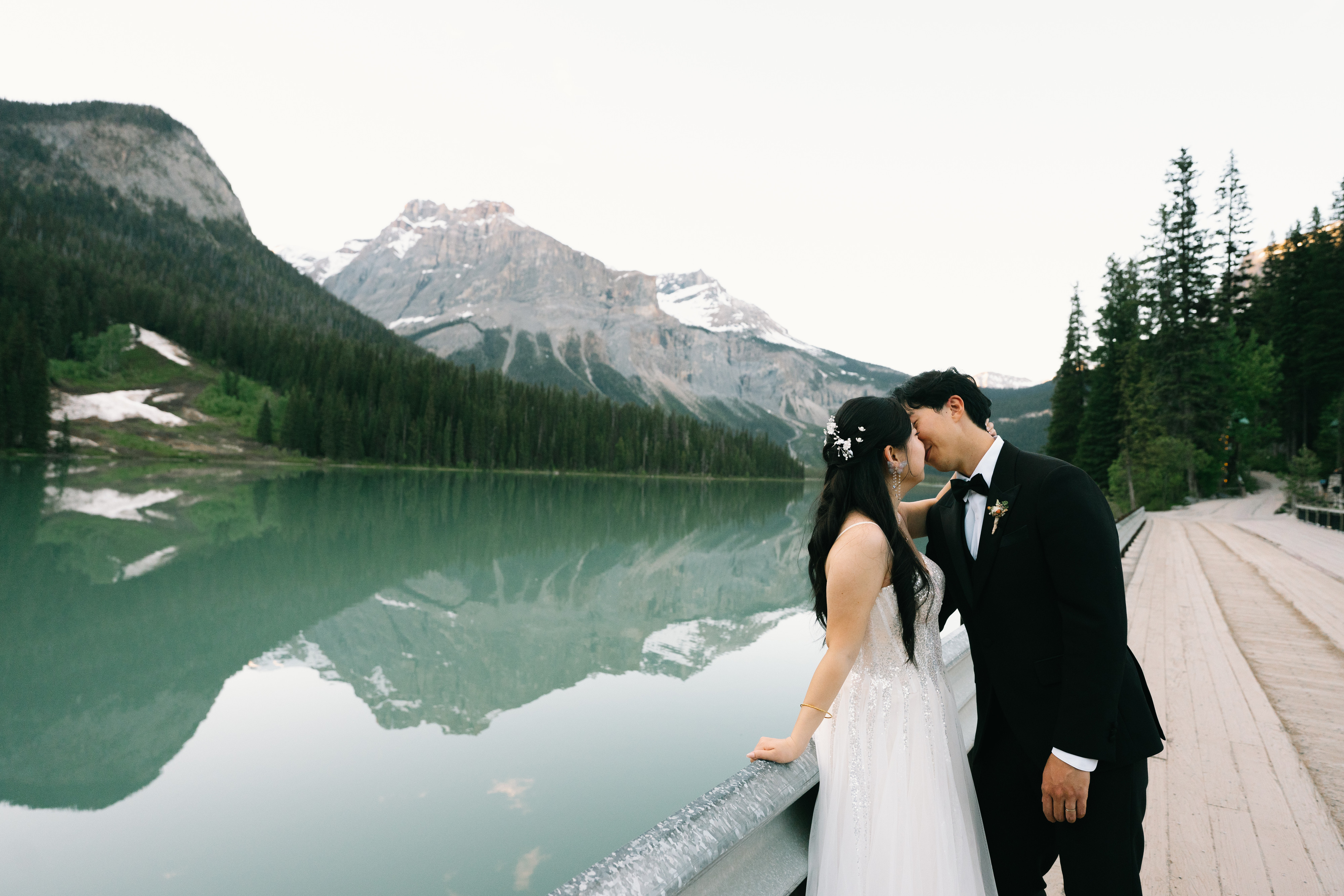 Newlyweds kissing beside Emerald Lake and its mountain reflections